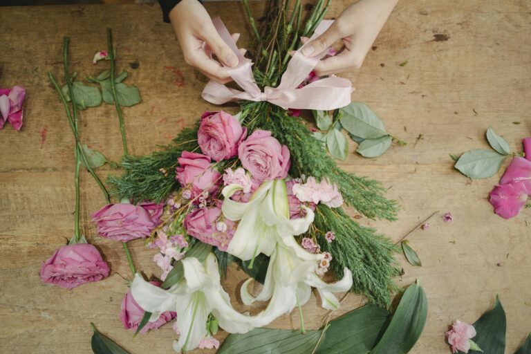 From above of crop anonymous woman tying bow on bouquet of fresh flowers placed on wooden table